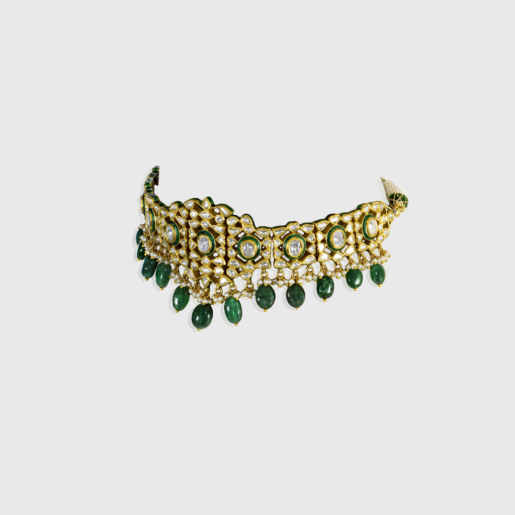 Embrace timeless elegance with this green Meena choker necklace and tops set, featuring sparkling uncut diamond polki, strung with vibrant emerald maniya and delicate pearls. Perfect for adding royal charm to any festive or bridal look.(KMNE3604)