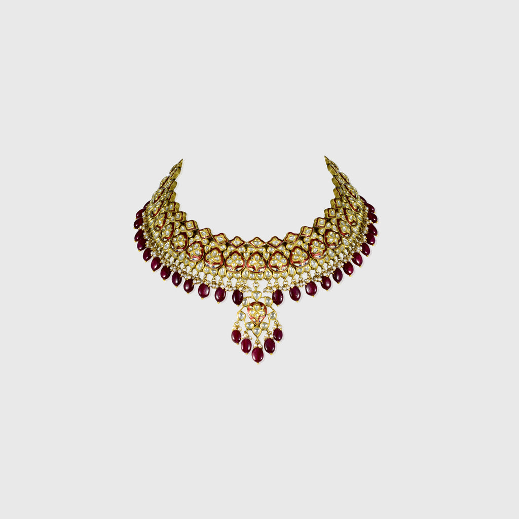 Beautiful red enameled flower design necklace and earrings set with sparkling uncut diamond polki, strung with ruby maniya and pearls. Perfect to add a touch of tradition and elegance to any special occasion.(KMNE3608)