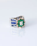 Featuring a diamond cluster center, encircled by vivid emeralds and accented with channel-set sapphires, this ring is designed to make a powerful statement. (PGDR0523)