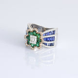 Featuring a diamond cluster center, encircled by vivid emeralds and accented with channel-set sapphires, this ring is designed to make a powerful statement. (PGDR0523)