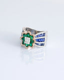 Featuring a diamond cluster center, encircled by vivid emeralds and accented with channel-set sapphires, this ring is designed to make a powerful statement. (PGDR0523)