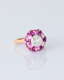 A radiant round diamond embraced by a halo of vivid pink sapphires—where timeless brilliance meets feminine charm. (PGDR0524)