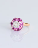 A radiant round diamond embraced by a halo of vivid pink sapphires—where timeless brilliance meets feminine charm. (PGDR0524)